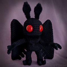 a crocheted black bat with red eyes on it's head and legs