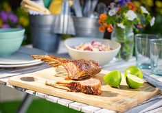 a wooden cutting board topped with meat next to a bowl of salad and limes