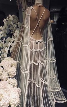 the back of a woman's dress with white flowers in front of it and behind her