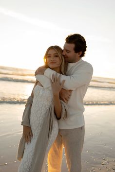 a man and woman hugging on the beach at sunset, with their arms around each other