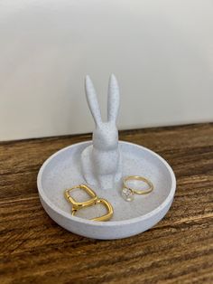 two gold rings are sitting in a white holder with a bunny's head on it