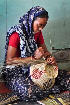 a woman sitting on the ground working on some kind of woven basket with grass in front of her