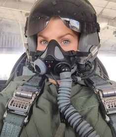 a woman wearing a gas mask and goggles in a fighter jet cockpit, with the pilot's helmet on