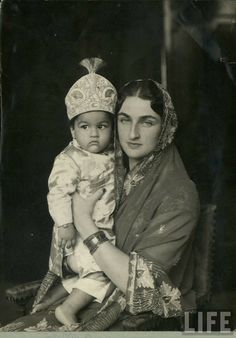 an old black and white photo shows a woman holding a baby in her arms, wearing a headdress