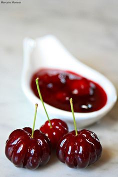 three cherries sit on a table next to a small bowl of ketchup