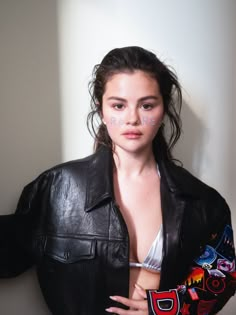 a woman wearing a black leather jacket and white bra posing in front of a wall