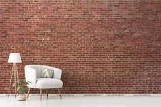 a white chair sitting in front of a brick wall with a lamp next to it