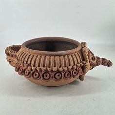 a clay pot with handles and decorative designs on the rim, sitting on a white surface