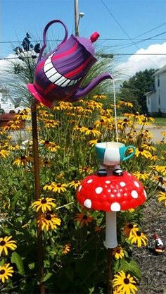 a garden with flowers and a tea pot on top of a mushroom shaped planter