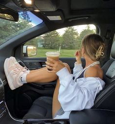 a woman sitting in the back seat of a car holding a drink