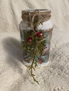 a glass jar filled with white sand and christmas decorations on top of a table cloth