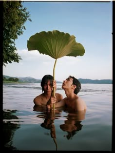 two people are in the water with a large leaf