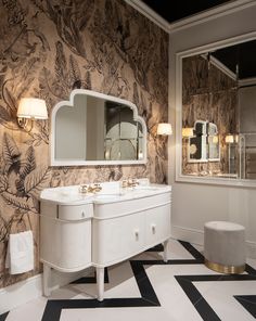 a bathroom with black and white tile flooring and wall papered walls, two vanity sinks and mirrors