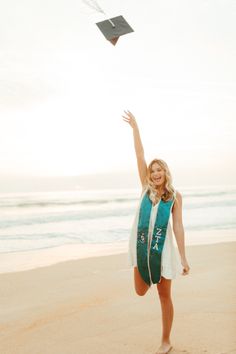 a woman on the beach flying a kite in the air with her hand up to the sky