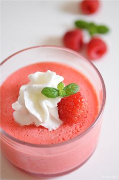 a small glass filled with fruit and cream on top of a white table next to raspberries