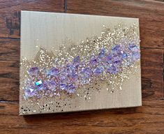 a painting with purple and silver glitters on it sitting on a wooden floor next to a wall