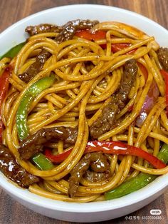 a white bowl filled with noodles and meat on top of a wooden table next to chopsticks