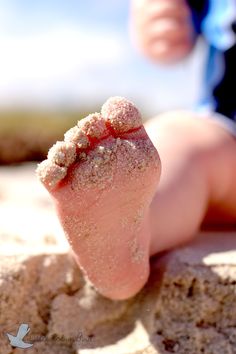 a baby's foot covered in sand on the beach