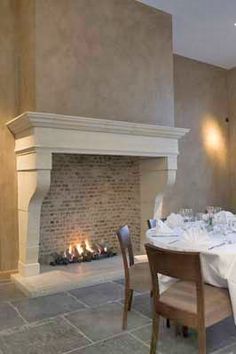 a dining room table set with white linens and place settings in front of a fireplace