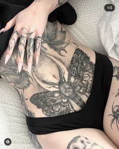 a woman laying on top of a bed with tattoos on her stomach and hands behind her back