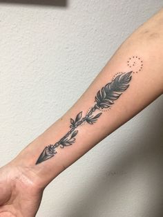 a woman's arm with an arrow and feathers tattoo on the left inner forearm