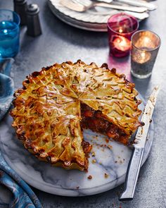 a pie sitting on top of a white plate next to a knife and some glasses