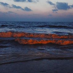 an ocean view with waves coming in to shore and the sun setting on the horizon