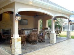 an outdoor kitchen and dining area is shown in this backyard setting with stone pillars, columns, and ceiling fan