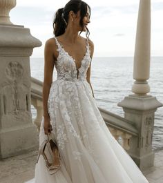 a woman in a white wedding dress standing on a balcony near the ocean with her handbag