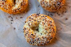 four bagels with sesame seeds and cheese on them sitting on a piece of wax paper