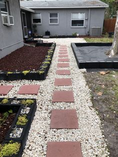 a walkway made out of bricks and gravel in front of a house with a tree