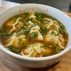 a white bowl filled with soup and noodles on top of a wooden table next to a cup of coffee