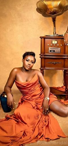 a woman in an orange dress sitting on the ground next to a table with a record player