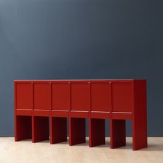 a red cabinet sitting on top of a hard wood floor next to a blue wall