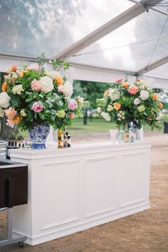 two vases filled with flowers sitting on top of a white counter under a tent