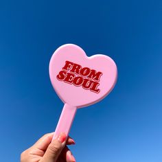 a pink heart shaped lollipop with the word from seoul on it in front of a blue sky