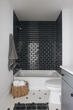 a white toilet sitting next to a bath tub under a bathroom window with black tiles