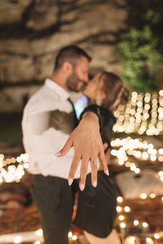 a man and woman are kissing in front of some lit up lights with their hands extended out