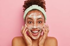 Smiling glad dark skinned young woman puts soap on face for cleansing, washes with cold water, wants to have healthy fresh skin., wears headband, looks positively at camera, stands naked indoor Brown Spots Removal, Micellar Water, Unclog Pores, Facial Cleansing, Wash Your Face, Face Cleanser, Dead Skin