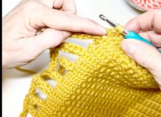 two hands crocheting the edges of a yellow knitted bag with blue yarn