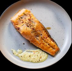 a piece of salmon on a white plate with mustard and seasoning next to it