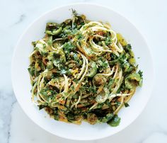 a white bowl filled with pasta covered in broccoli and sauce on top of a marble counter