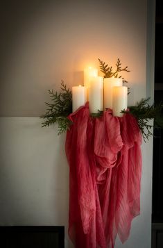 three candles are lit on the mantle with red tulle around it and greenery