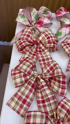 some red and green plaid bows are on a white table cloth with gold pins in the center