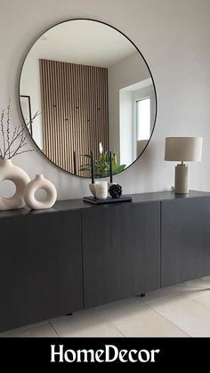 a large round mirror sitting on top of a wooden cabinet next to a lamp and vase