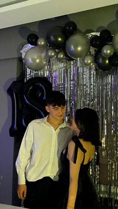 a young man and woman standing next to each other in front of some silver balloons