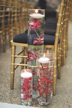 two tall vases filled with flowers and candles on top of a table next to chairs