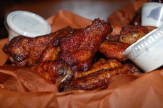 chicken wings with dipping sauce in a bowl on top of brown paper wrappers,