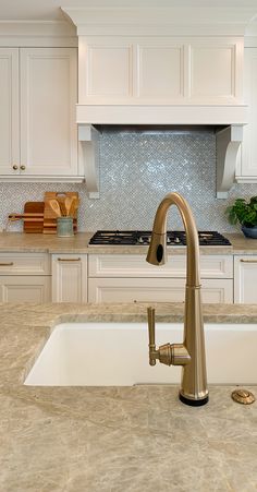 a white kitchen with marble counter tops and an island style sink in the foreground