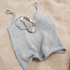 a knitted piece of clothing lies on the sand, with beads hanging from it